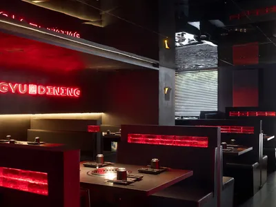 Empty modern restaurant interior with black walls, red accents on tables, and dining tables and chairs throughout