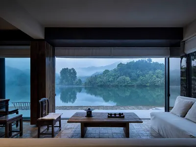 Cozy indoor living area with a large window overlooking a lake, featuring two couches, a dining table, and chairs, with a focus on relaxation and enjoying the view outside