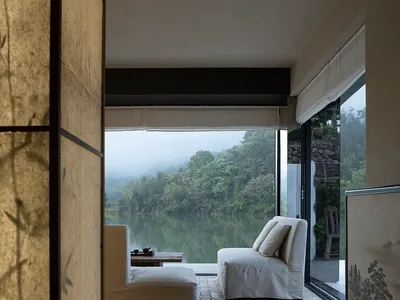 寬敞舒適的客廳空間，擺放沙發、椅子與茶几，面向大片窗戶，飾以亞洲藝術品且採光充足