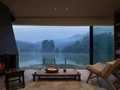 Cozy living area with a wooden table, chairs, and couch, overlooking a lake through a large window