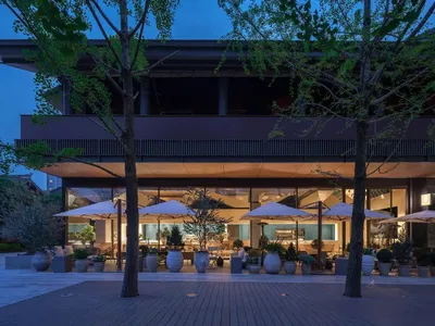 Outdoor dining space with tables, chairs, umbrellas, and a mix of wood and metal materials under dim warm lighting