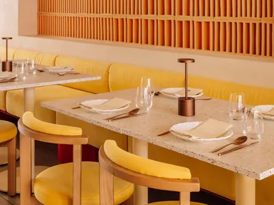 Modern restaurant interior with wooden panel walls, tables, chairs, and couches, featuring wine glasses and a stylish atmosphere