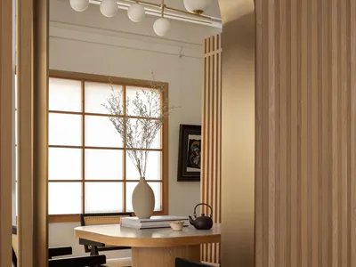 Cozy living space with wooden walls and floors, multiple chairs, benches, and a dining table, with a vase adding a decorative touch