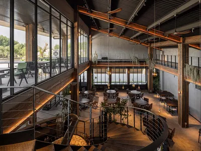 Spacious dining area with multiple tables and chairs, high ceilings, and large windows allowing natural light to fill the room