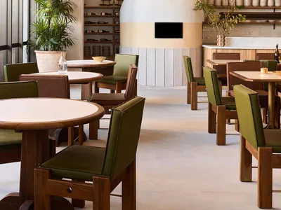 Cozy modern restaurant dining area with a stone oven, wooden tables, and vases, surrounded by chairs and warm lighting