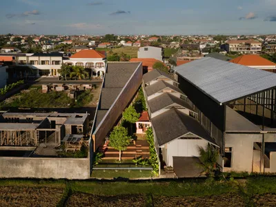 一座現代飯店與住宅透過橋樑相連，周圍環繞盆栽植物與座椅，混凝土外觀營造溫馨氛圍