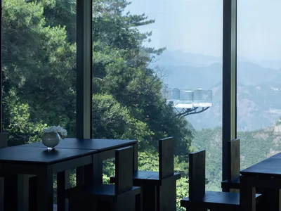 A restaurant interior with a dining area featuring multiple tables and chairs, a vase, and a mountainous backdrop