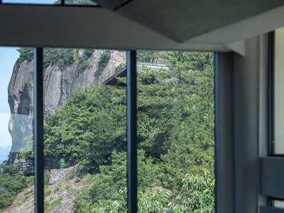 A modern restaurant with glass walls and wooden elements, offering a view of mountains in the distance through large windows