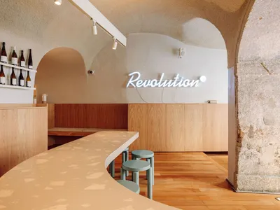 Modern restaurant bar with a counter and chairs, featuring bottles and a mix of natural and artificial lighting