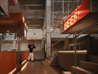 A modern restaurant and bar area with a woman walking down a hallway between two staircases, surrounded by bottles and stylish decor