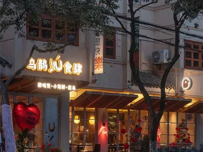A white building with red accents and outdoor seating area with potted plants, creating a warm and inviting atmosphere at night