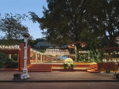 A red brick restaurant with outdoor seating and potted plants, set amidst a tree, creating a welcoming atmosphere