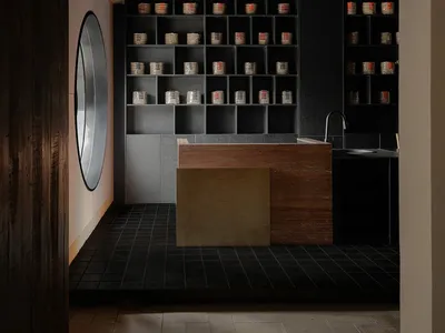 A cluttered bathroom with a black and white color scheme, featuring a sink, mirror, and various containers and bottles on the countertop