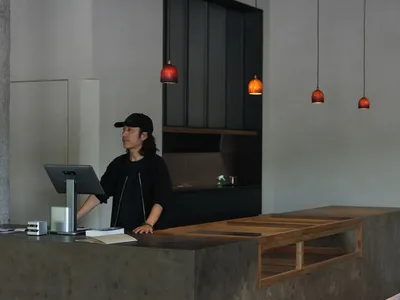 A modern restaurant interior with a counter area, concrete walls, wooden elements, and pendant lights