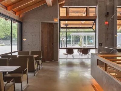 Modern restaurant interior with wood accents, concrete flooring, and potted plants, featuring a large dining area with multiple chairs and tables
