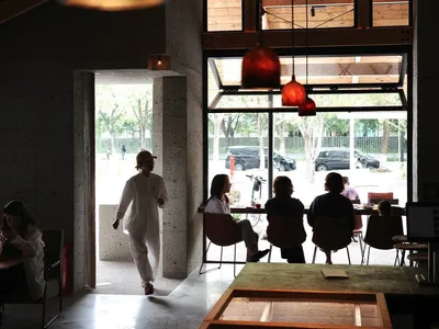 A casual indoor space with concrete walls, dining tables, chairs, and bicycles, featuring people enjoying a relaxed atmosphere