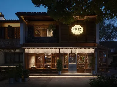 Asian restaurant with a wooden exterior, large window, and potted plants, featuring multiple dining tables and chairs in a comfortable atmosphere