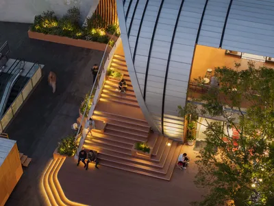 A casual meeting space with a staircase, people sitting on benches, and potted plants adding greenery to the environment
