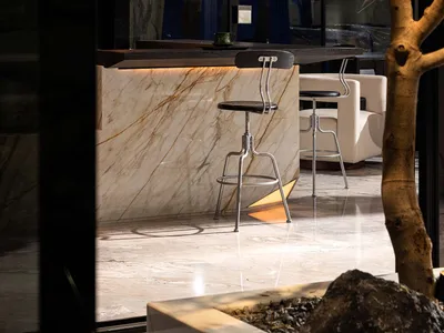 A well-lit living area with a marble kitchen counter, stools, chairs, and a comfortable atmosphere