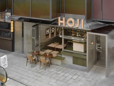 Outdoor restaurant with a modern design featuring a bar area, chairs, and dining tables, with wine bottles adding to the ambiance