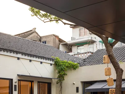 一個溫馨的庭院餐廳區域，配有木椅、餐桌與盆栽植物，位於大型建築群內