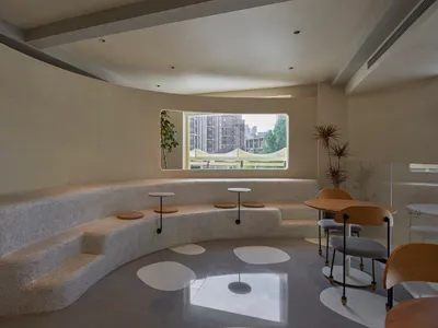 A well-lit room with a curved bench and chairs, three round tables, and a window, creating a comfortable and inviting atmosphere for socializing or dining