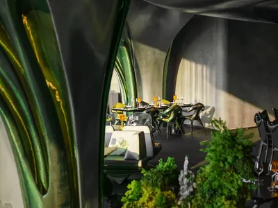 Casual restaurant dining area with multiple tables, chairs, and potted plants, with backpacks on some chairs