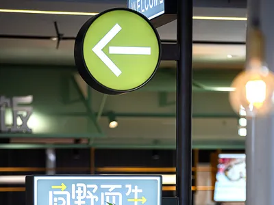A well-lit Asian restaurant with a green sign featuring Chinese characters, surrounded by potted plants and two TVs on the wall