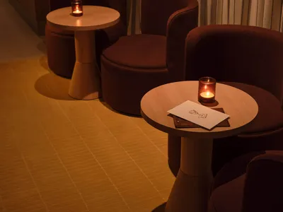 A well-lit restaurant dining area with three brown chairs around a table, a menu displayed, and warm lighting creating an inviting atmosphere