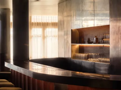 A modern bar area with a large wooden counter featuring a marble top, wine glasses, and bottles, set in a sophisticated and inviting atmosphere