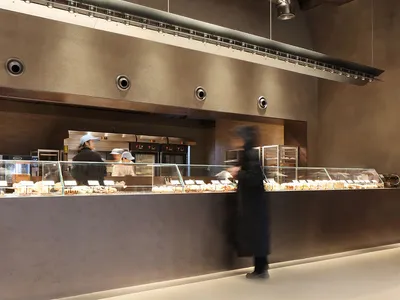 繁忙的商業廚房，有兩人準備餐點與甜點，周圍陳列多款蛋糕
