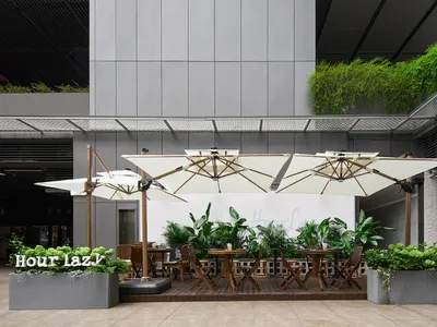 A restaurant patio with tables, chairs, and umbrellas surrounded by potted plants, creating a welcoming atmosphere for outdoor dining