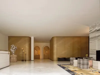 Spacious hotel lobby with a checkered rug, gold accents, two couches, chairs, a dining table, and decorative vases