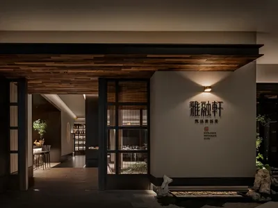 A modern Asian restaurant with a large dining area, potted plants, artwork, and wooden flooring, creating a cozy atmosphere
