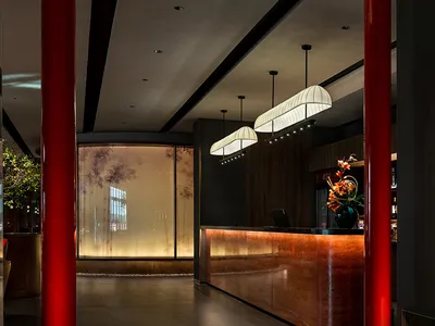 Modern hotel lobby with a red pillar, wood, and glass elements, two potted plants, and inviting atmosphere