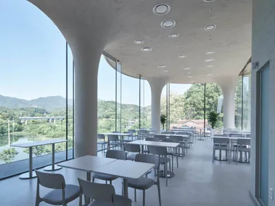 Modern restaurant interior with multiple tables, booths, and chairs, featuring clean lines, minimal decoration, and warm lighting
