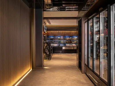 Dimly lit store with a refrigerator in the background, wooden chairs, and bottles on display