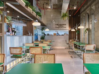 Empty restaurant interior with green tables and chairs, white and red walls, and potted plants, creating a clean and organized atmosphere
