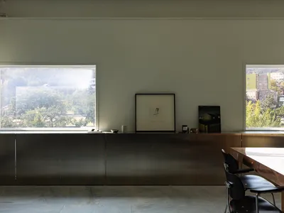 Empty living room with a large window, two chairs, a dining table, and a vase, with sunlight entering the space