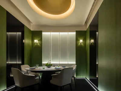 A dining area with a round table, four chairs, and various table settings in a modern restaurant with green walls and good lighting