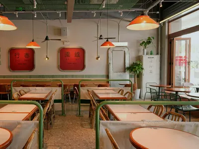 A modern Asian restaurant with a long dining table and multiple chairs, surrounded by tables with green accents on the walls and floors, creating an inviting and comfortable atmosphere
