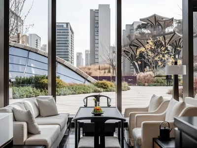 A well-lit indoor living area with a large window offering a city view, featuring two couches, a dining table, chairs, and decorative accents