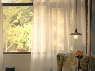Cozy living space with a chair, cushion, and dining table, surrounded by books and a vase, in front of a window