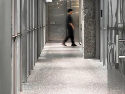 A modern hotel lobby with a silver metal finish, featuring two individuals walking down the hallway