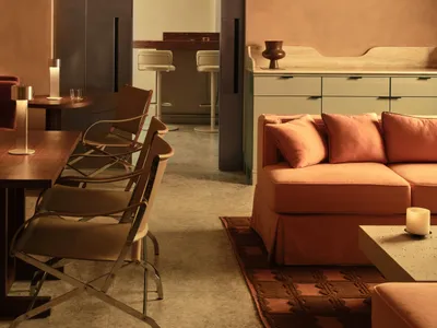 A modern living space with a large couch, dining table, chairs, kitchen area, refrigerator, and sink, featuring a warm and inviting atmosphere