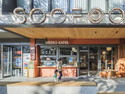 A casual outdoor cafe with a wooden exterior, a dining table, and chairs, surrounded by people in a relaxed atmosphere