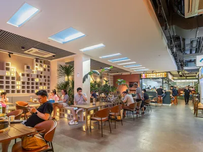 A casual dining area in a restaurant with wood and metal elements, featuring tables and chairs, patrons enjoying meals and conversation