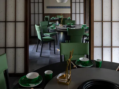 A modern restaurant interior with Asian-inspired decorations, dark wood flooring, and dim lighting, featuring tables, chairs, and tableware