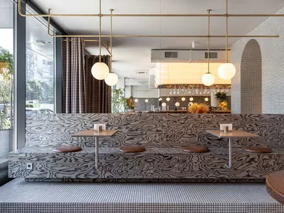 Modern restaurant interior with a bar, dining table, chairs, and unique patterned walls, accented with bottles and ambient lighting