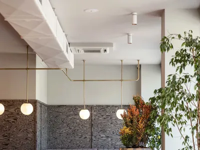 A modern restaurant dining area with multiple tables, chairs, and potted plants, featuring grey walls and wooden furniture